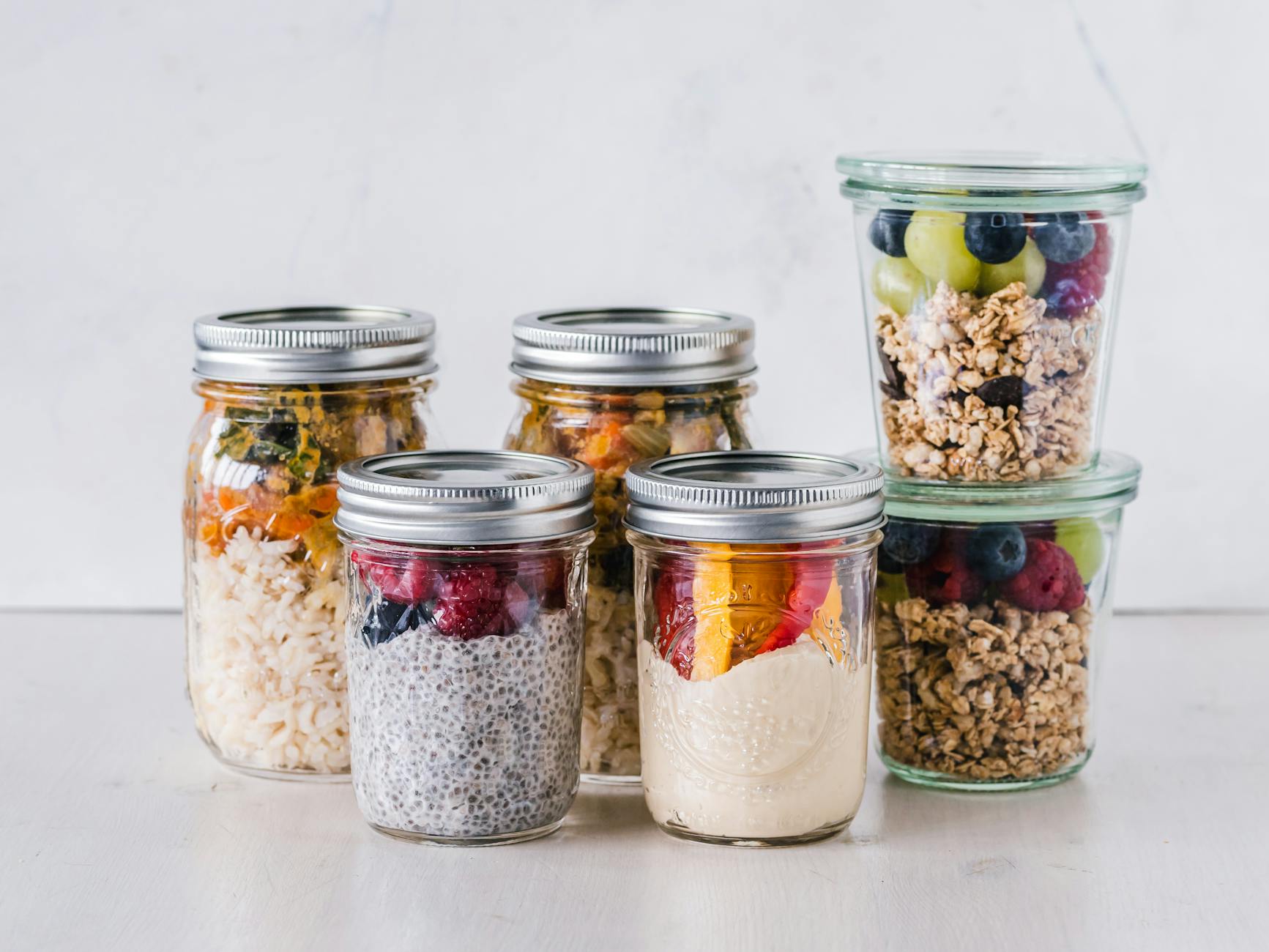 six fruit cereals in clear glass mason jars on white surface